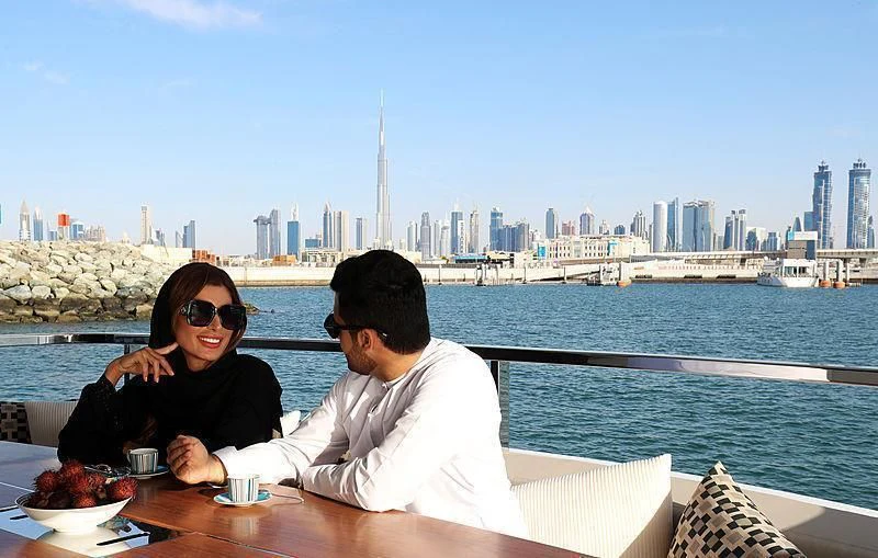 a man and a woman sitting at a table with food in front of a city skyline aboard MAXIMUS Yacht for Sale