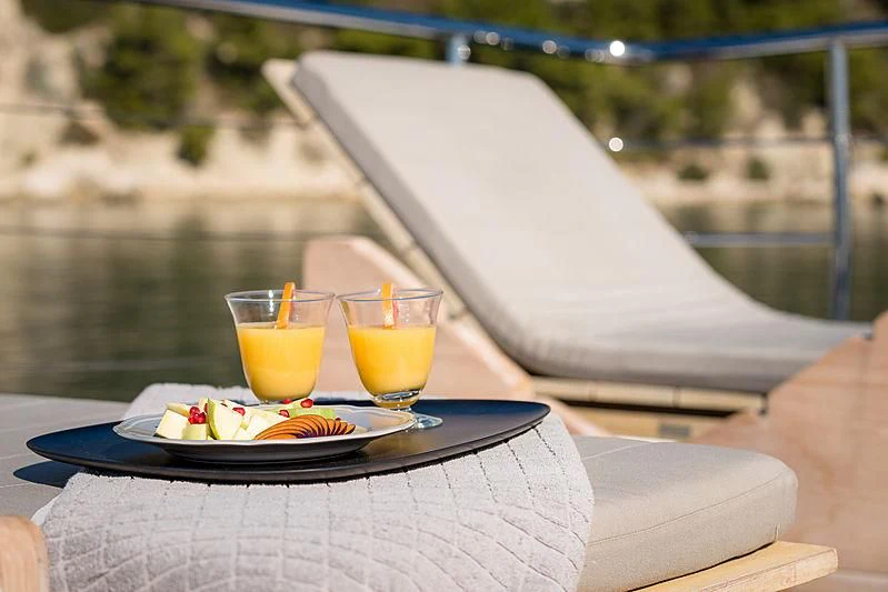 a table with a plate of food and glasses of juice on it aboard MOONRAKER II Yacht for Sale