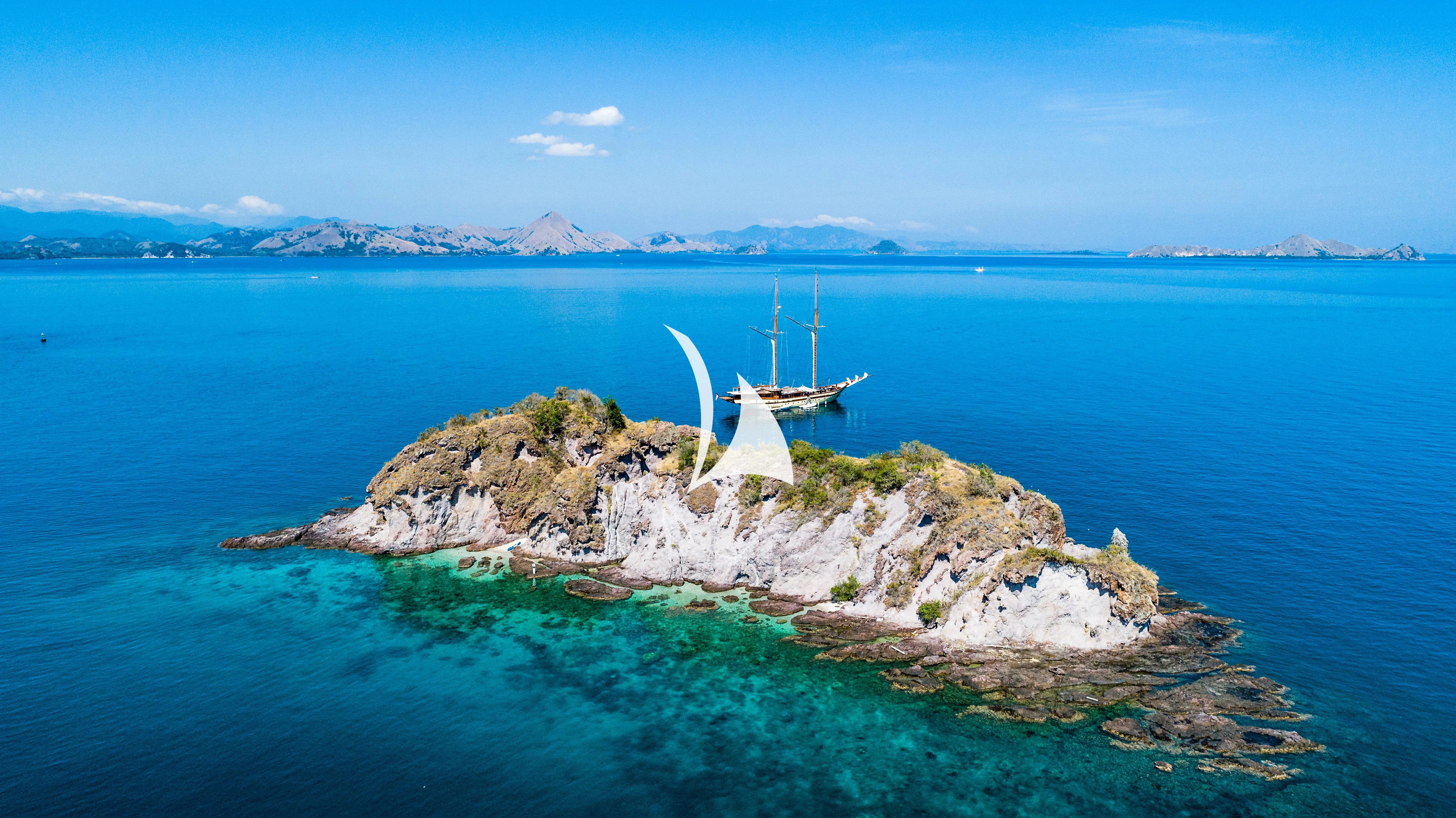 a white sailboat on a rocky island surrounded by water aboard LAMIMA Yacht for Sale