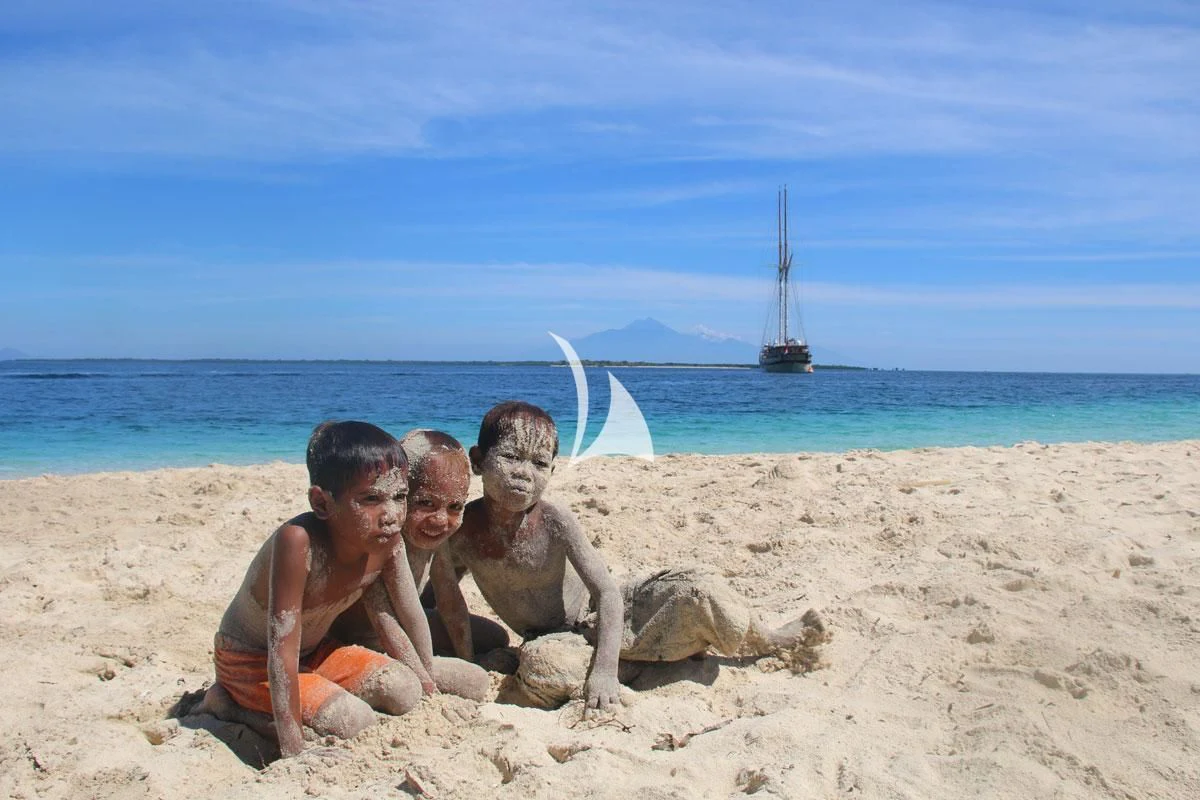 a group of people sitting on a beach with a sailboat in the background aboard LAMIMA Yacht for Sale