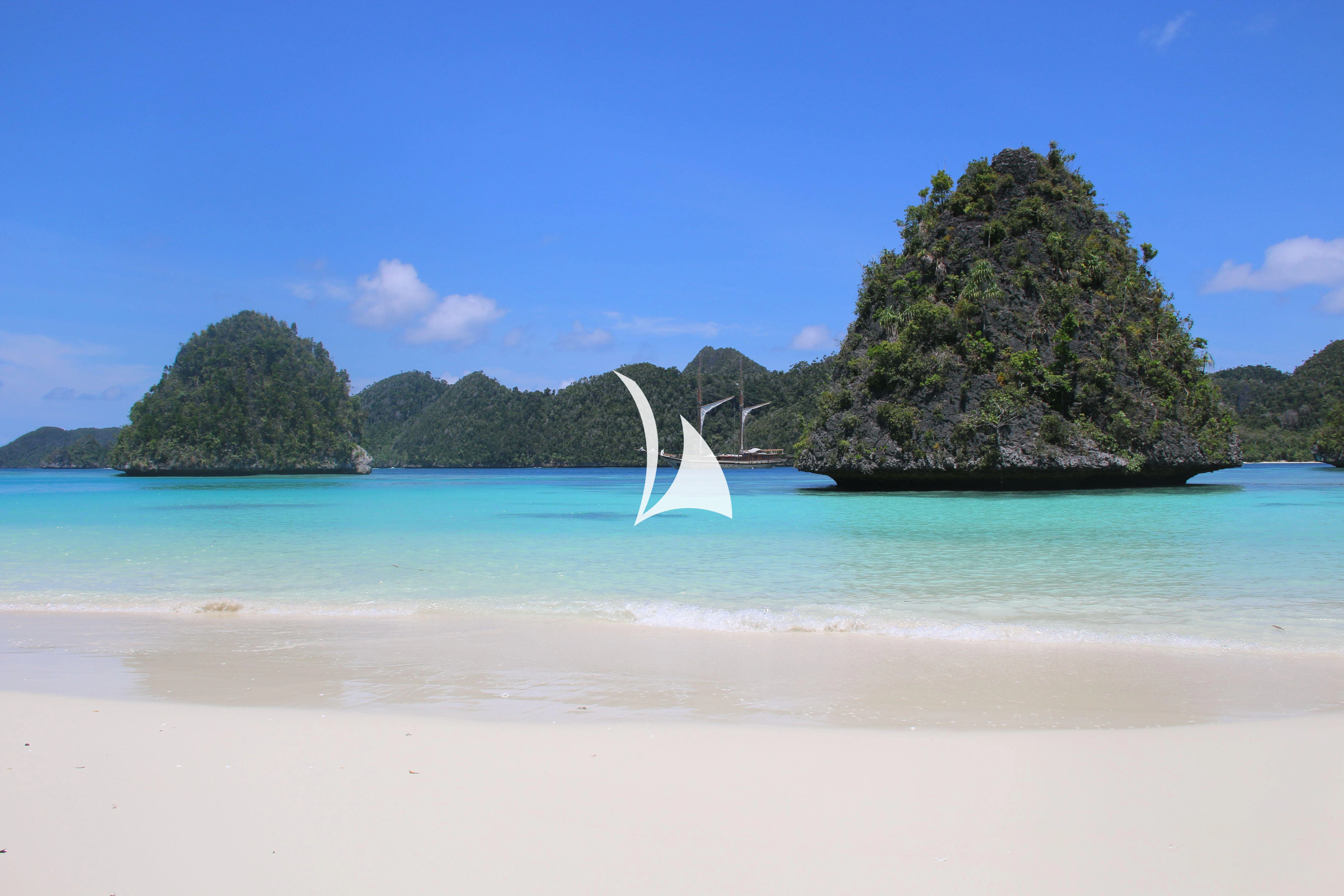 a body of water with a white sand beach and trees in the background aboard LAMIMA Yacht for Sale