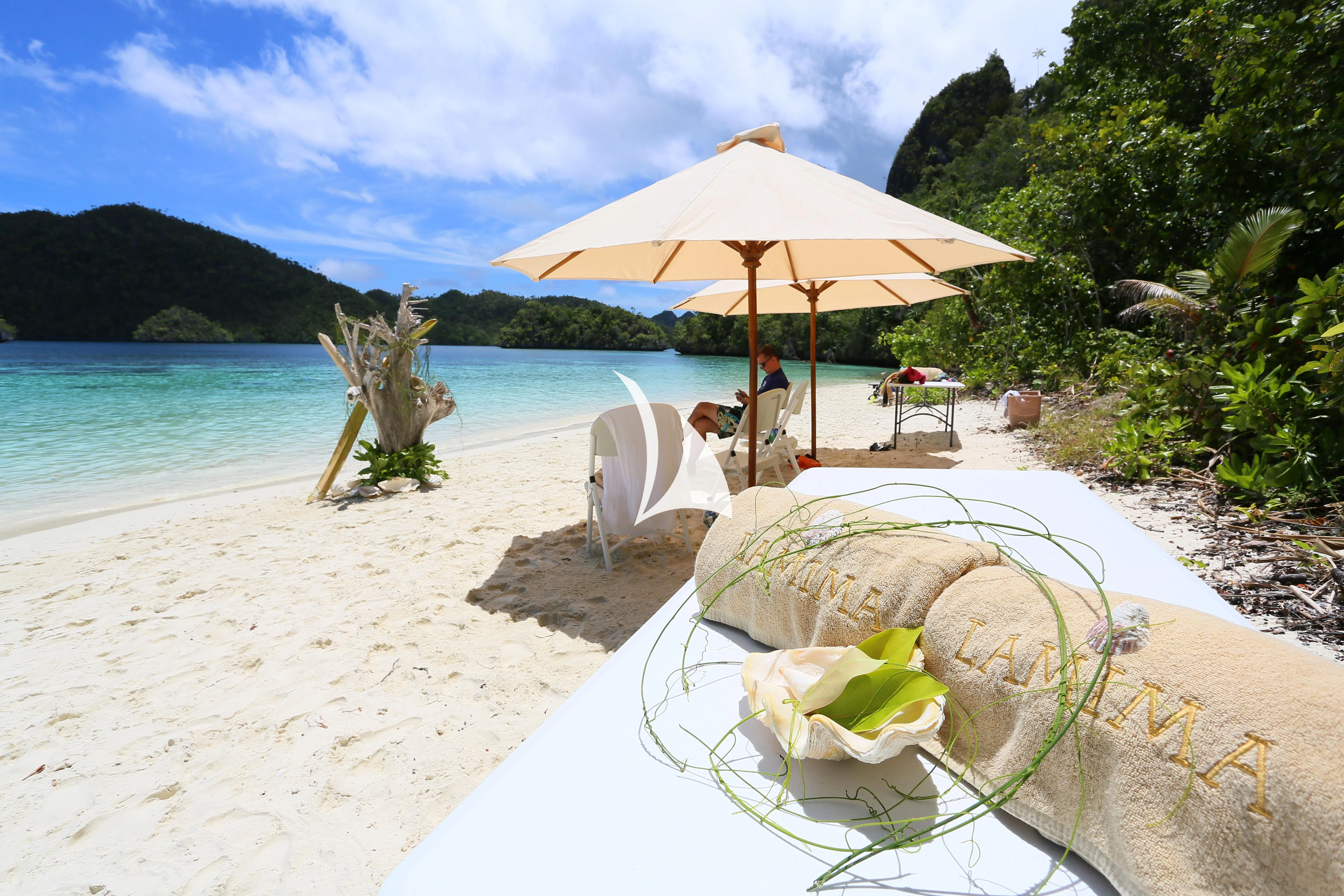 a table with a chair and umbrella on a beach aboard LAMIMA Yacht for Sale