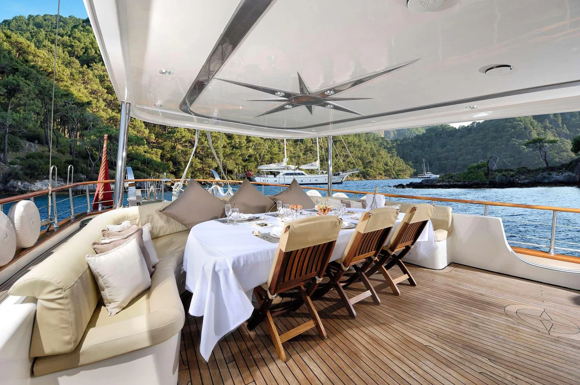 a room with a table and chairs on a deck with a body of water and trees in the aboard ALESSANDRO I Yacht for Sale