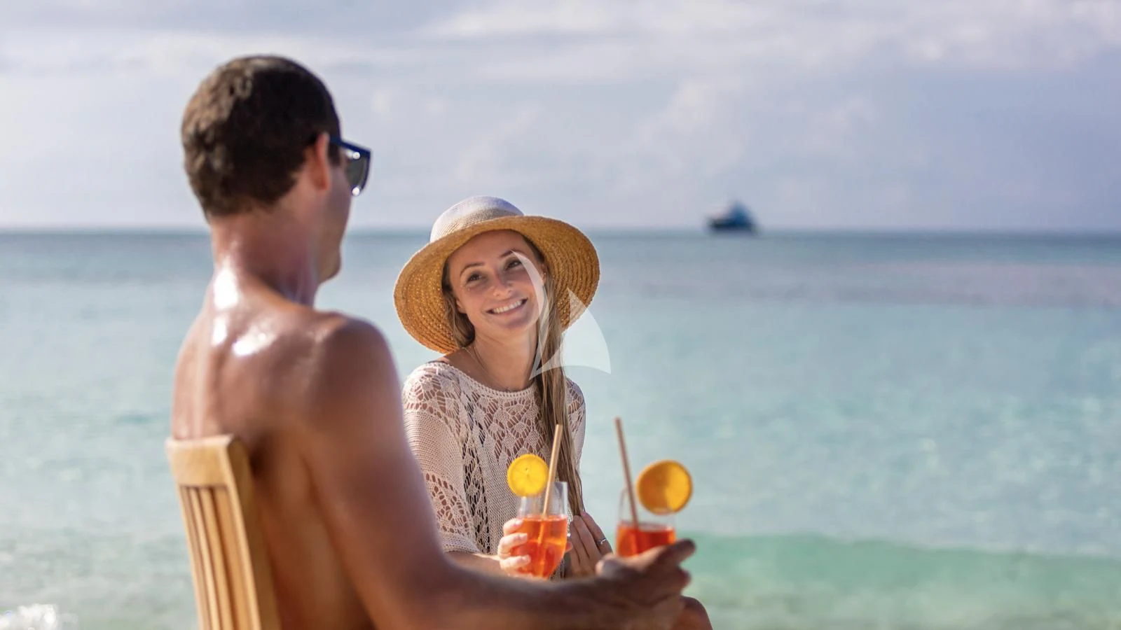 a man and woman sitting on a beach with a drink and a straw aboard LAUREL Yacht for Charter