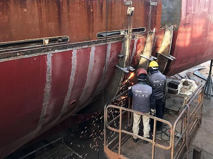 a few men wearing hard hats working on a large red pipe aboard COMMITMENT Yacht for Sale