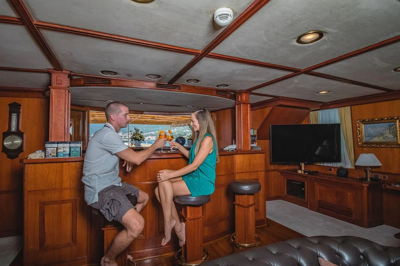 a man and woman sitting on stools in a room with a television and a table and chairs aboard SEAGULL II Yacht for Sale