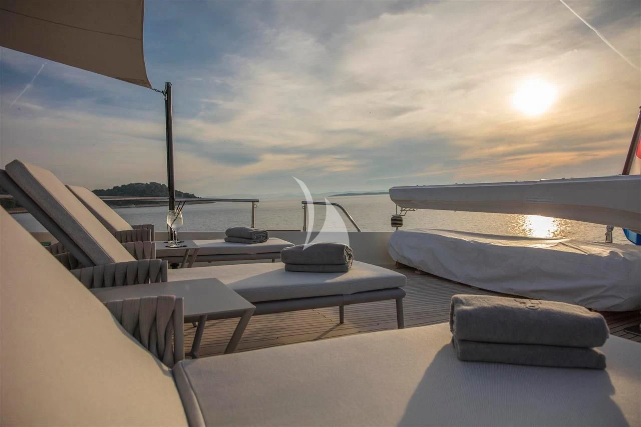 a lounge area with a large white lounge chair and a large body of water and a sunset in aboard ENA Yacht for Sale