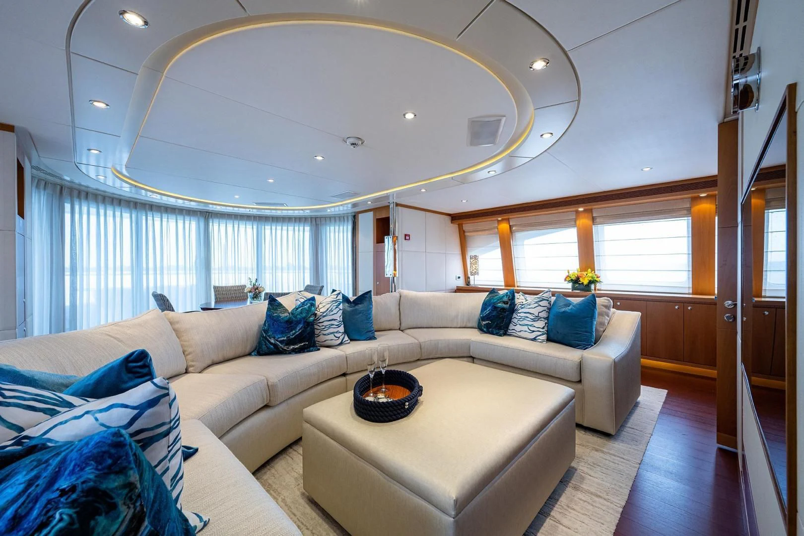 a living room with a large white sofa and a round table with blue pillows and a white table aboard SHARKFINN Yacht for Sale