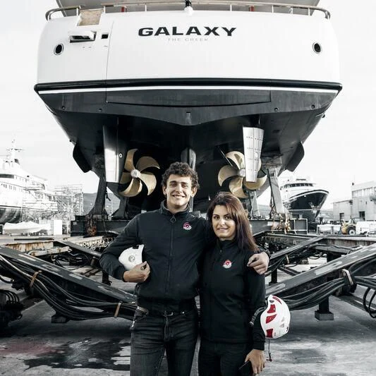 a group of people posing for a picture in front of a large ship aboard GALAXY Yacht for Sale