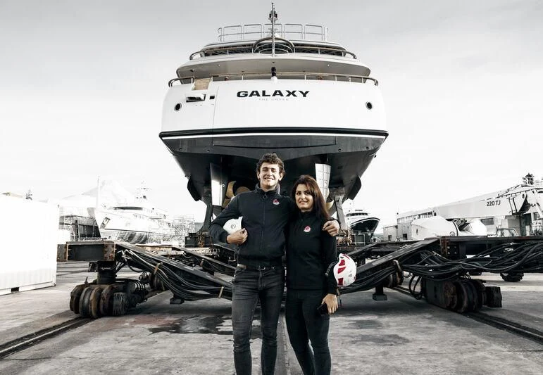 a man and woman posing in front of a large ship aboard GALAXY Yacht for Sale