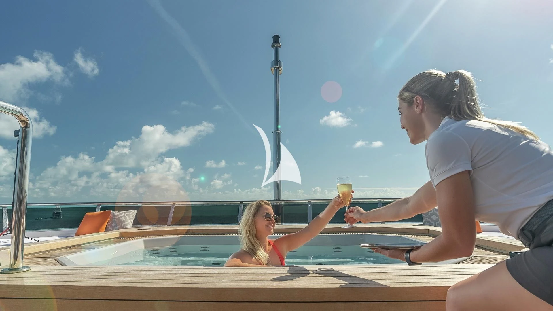 a couple of women sitting on a deck with drinks and a sailboat in the background aboard ODESSA Yacht for Sale