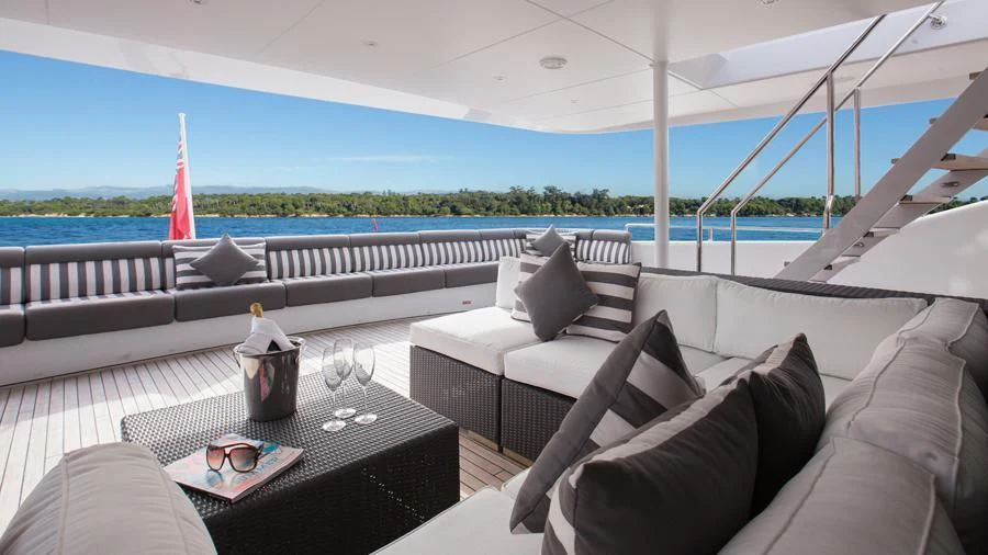 a large white sofa with a table and a glass of wine on a table with a view of aboard BENIK Yacht for Charter