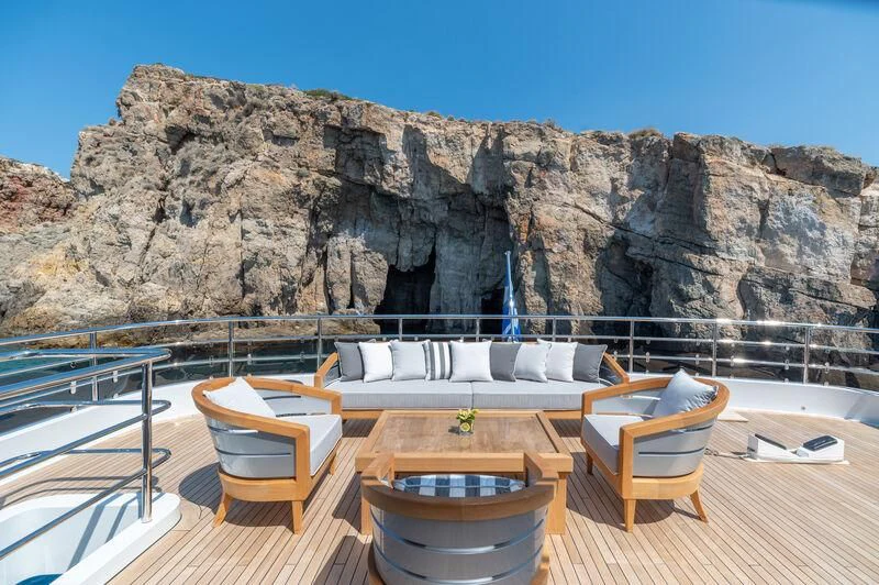 a deck with chairs and a rock mountain in the background aboard BOJI Yacht for Sale