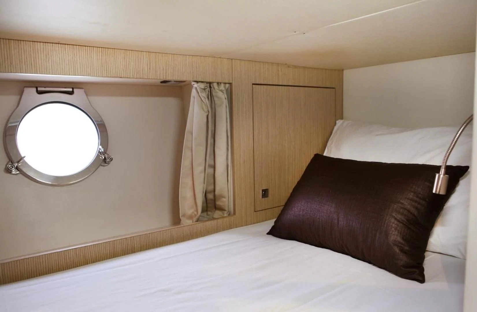 a bed with a white sheet and a round window aboard KUDU Yacht for Sale