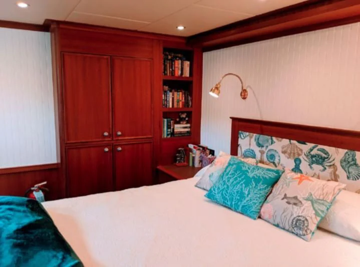 a bed with pillows and a bookcase aboard IIWII Yacht for Sale