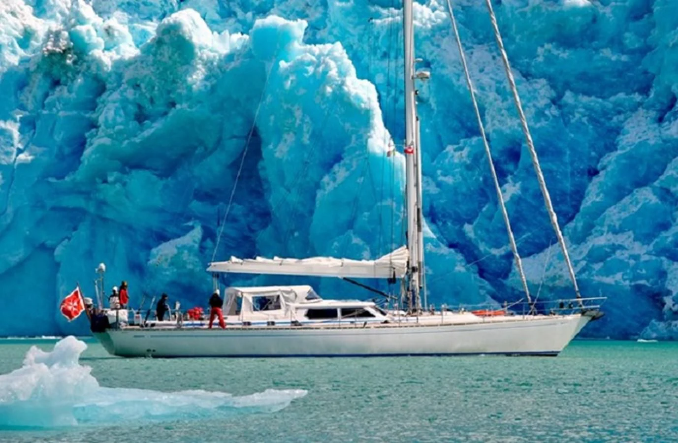 a boat with a sail on the water with a large waterfall behind it aboard PLUM Yacht for Sale