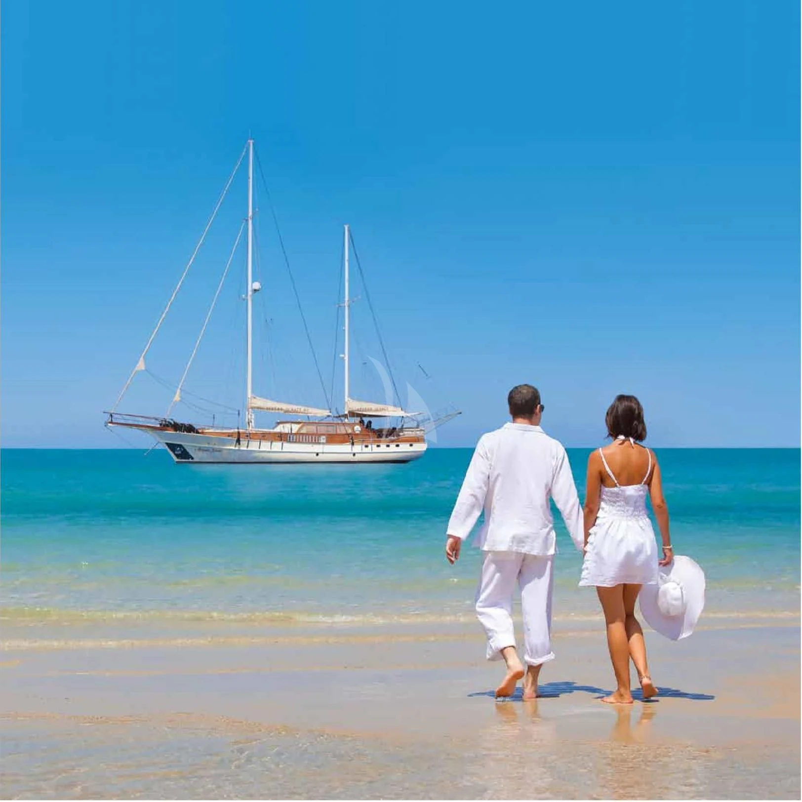a man and woman walking on a beach with a sailboat in the background aboard SCHATZ Yacht for Sale