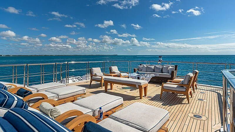 a deck with chairs and tables on it by the ocean aboard ANDIAMO Yacht for Sale