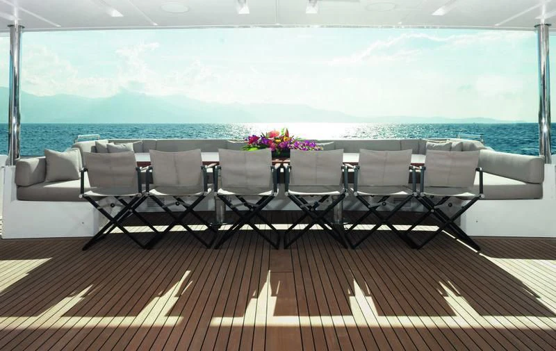 a table set with chairs and flowers on a deck overlooking a body of water aboard EMINA Yacht for Charter