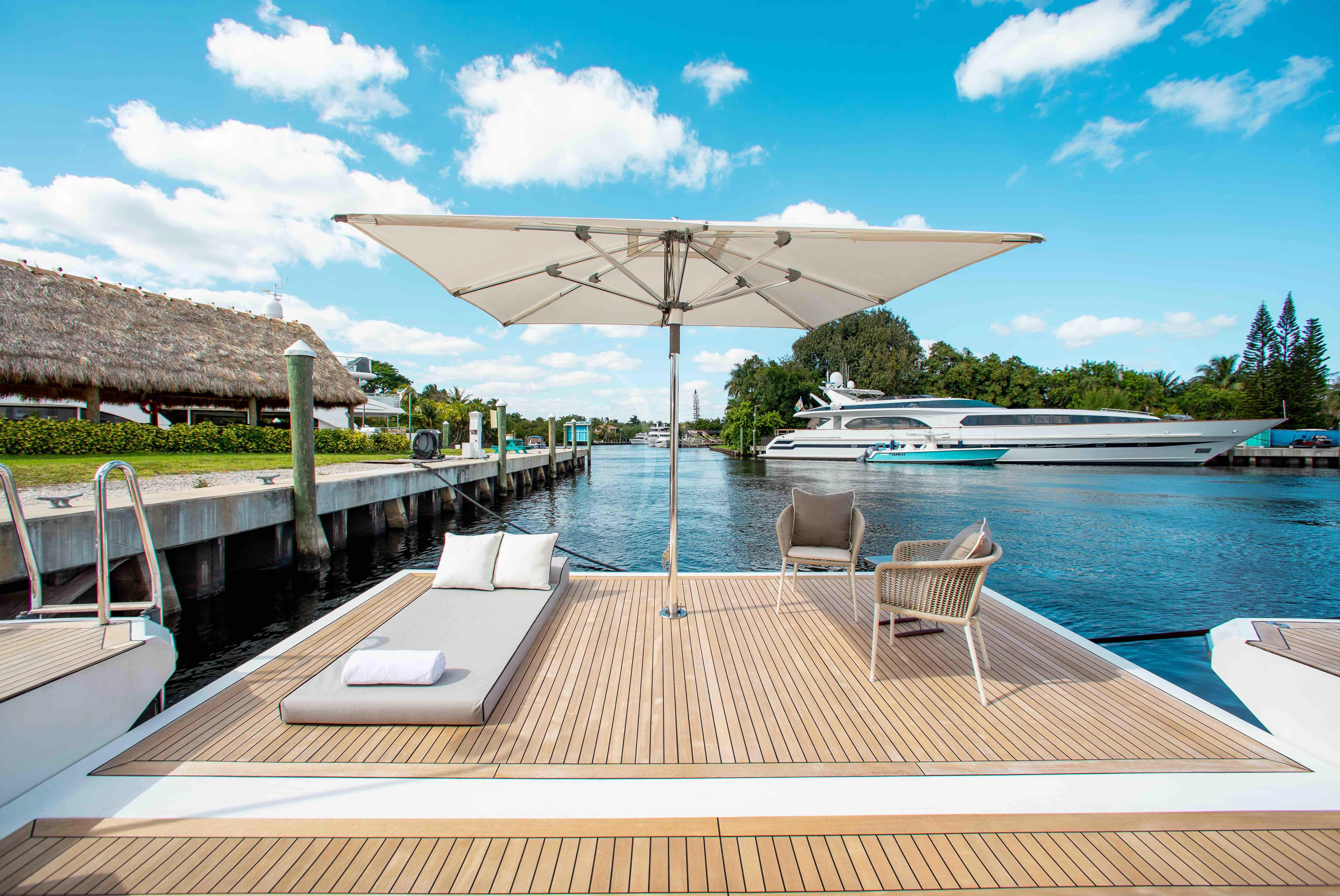 a deck with chairs and a table on it by a body of water aboard EMINA Yacht for Charter