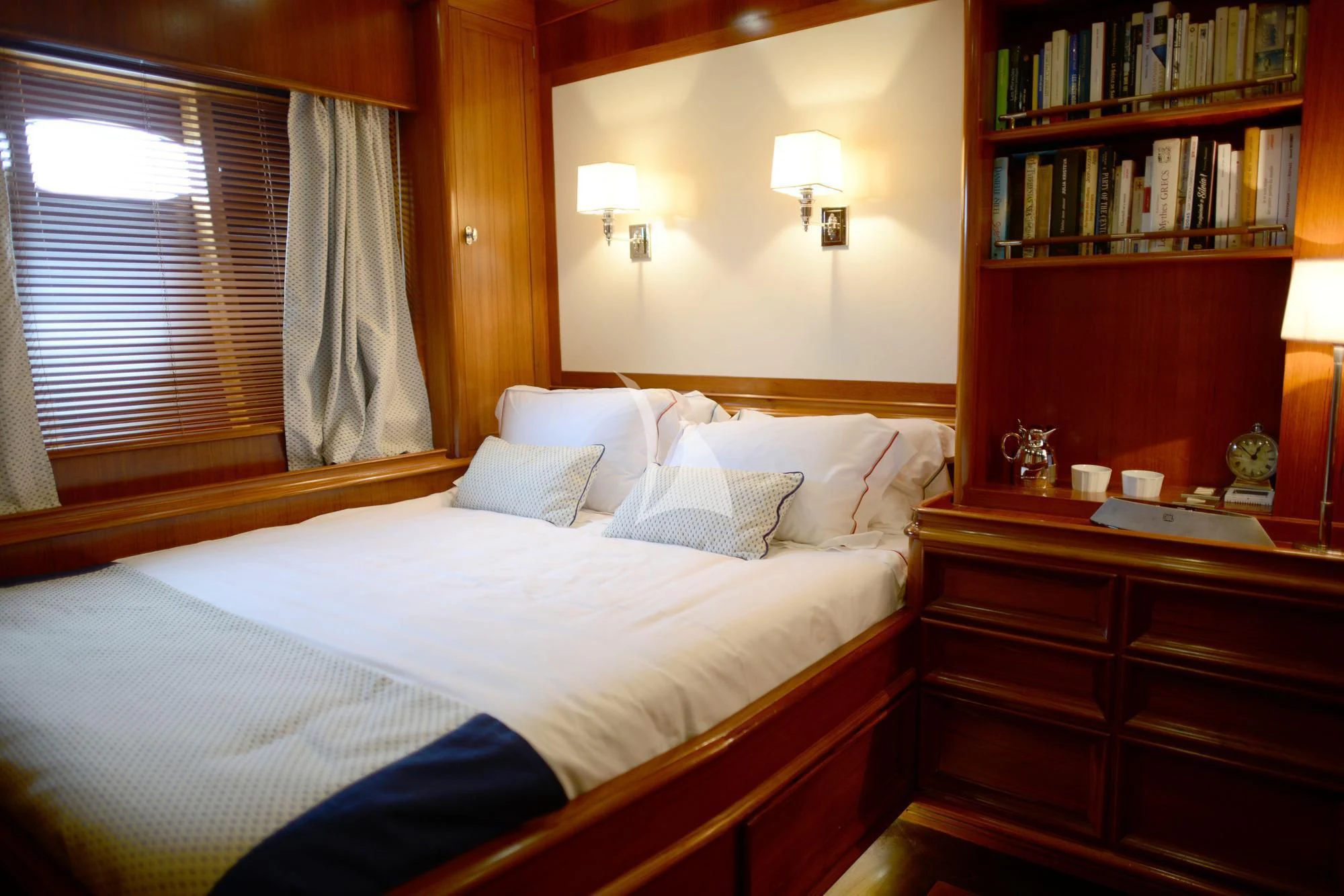 a bed with a white sheet and pillows in a room with a bookcase and a window aboard EUGENIA VII Yacht for Sale