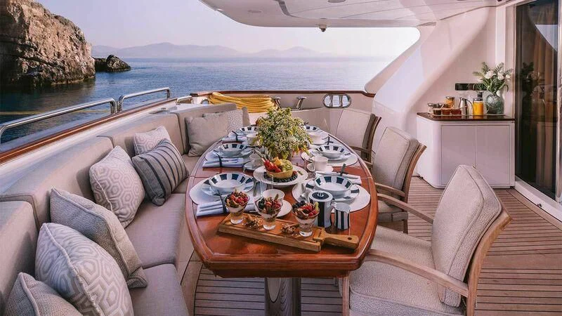 a table with a couch and a pool in the background aboard OAK Yacht for Charter