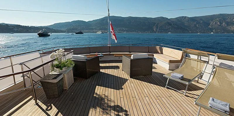 a deck with chairs and a flag on it by the water aboard SHAHA Yacht for Sale