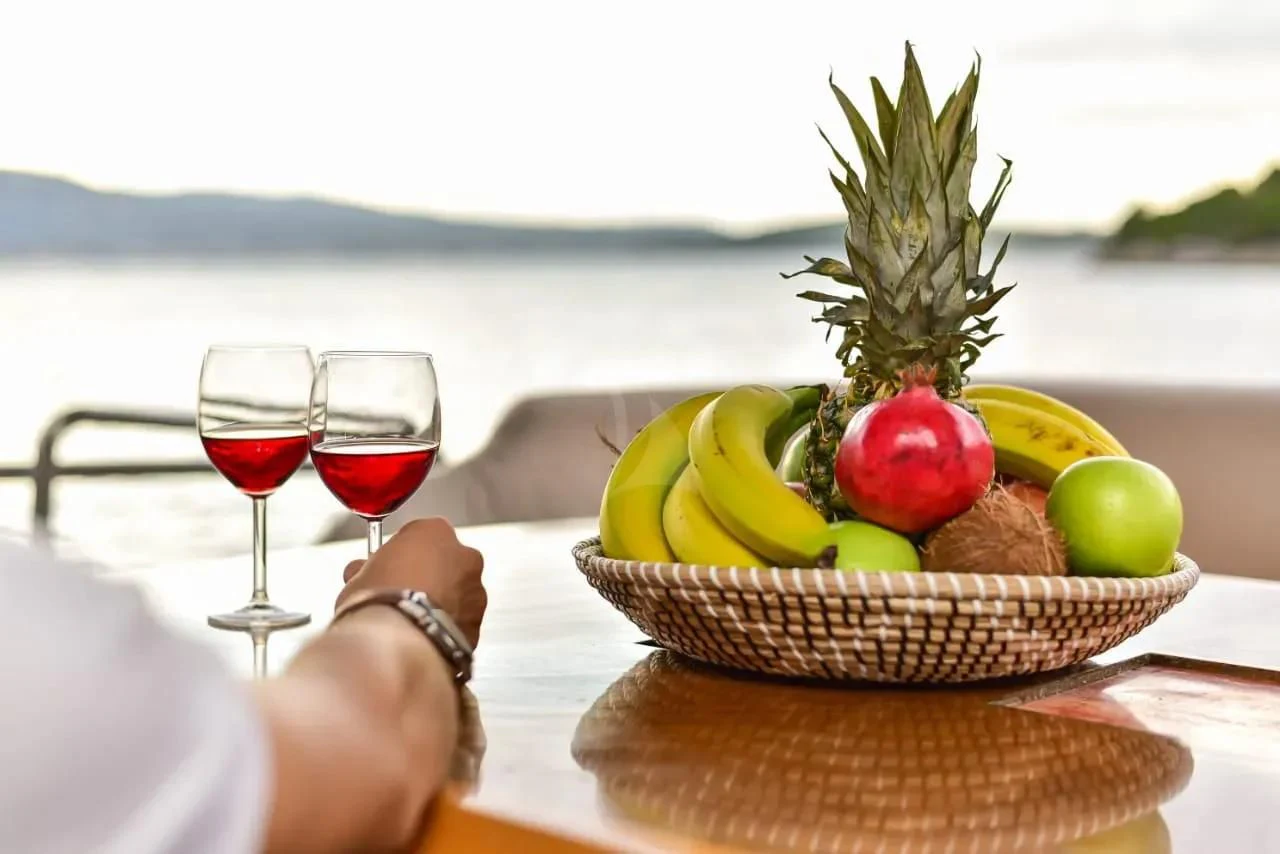 a basket of fruits and a glass of wine on a table aboard STELA 117 Yacht for Sale