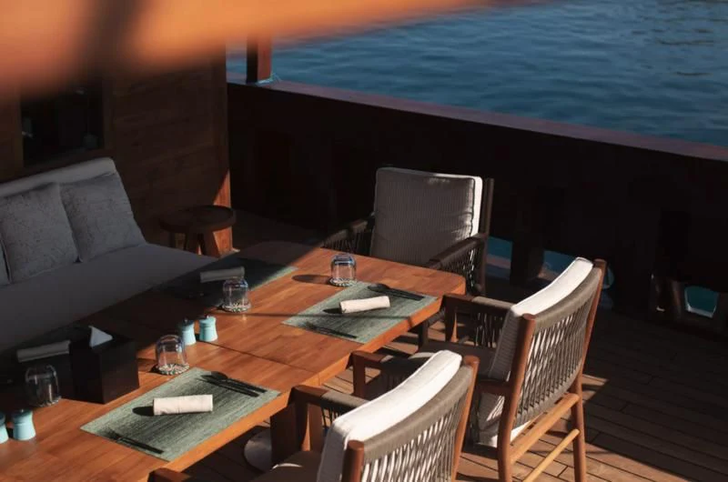 a table with chairs and a boat in the background aboard VELA Yacht for Charter
