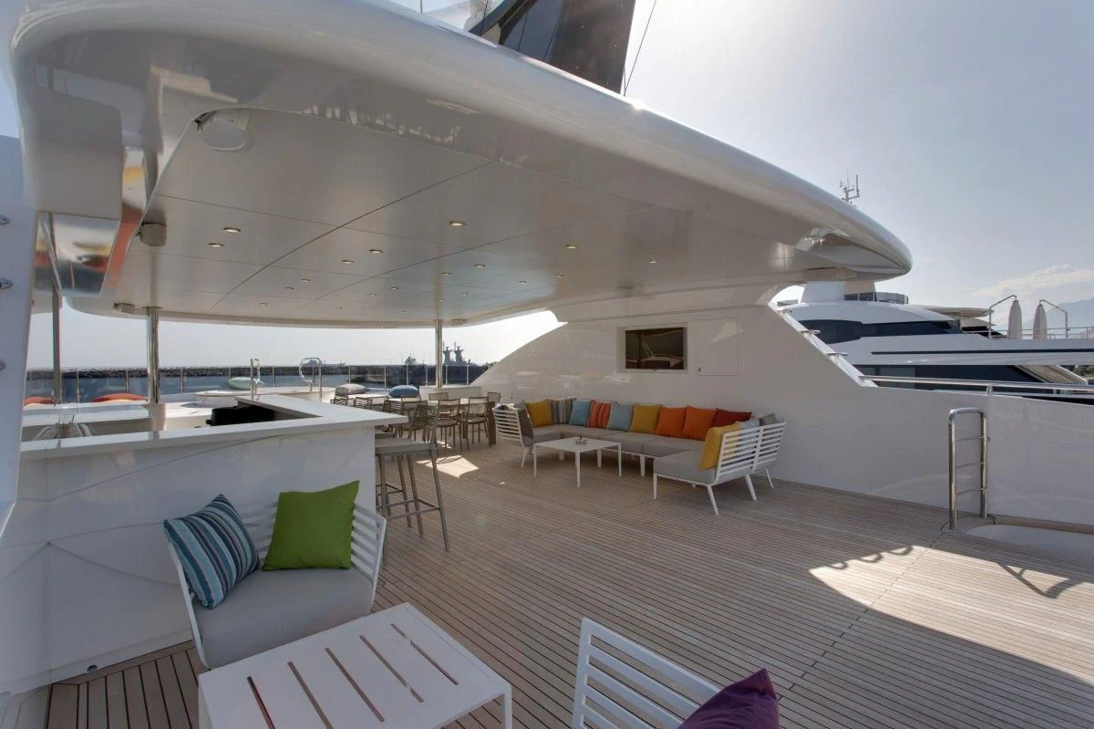 a lounge area with a boat and a deck with chairs and tables aboard BEBE Yacht for Sale