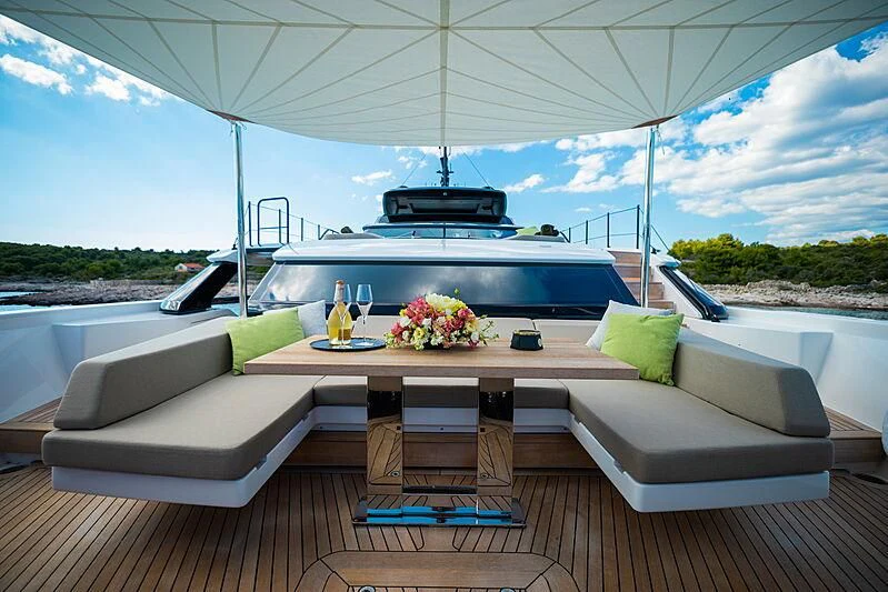 a white couch with a table and chairs on a deck with a view of the water and blue aboard NOOR II Yacht for Charter