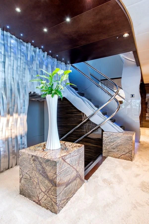 a vase with flowers on a stone stand in a room with a blue curtain and a staircase aboard TIAMAT Yacht for Sale