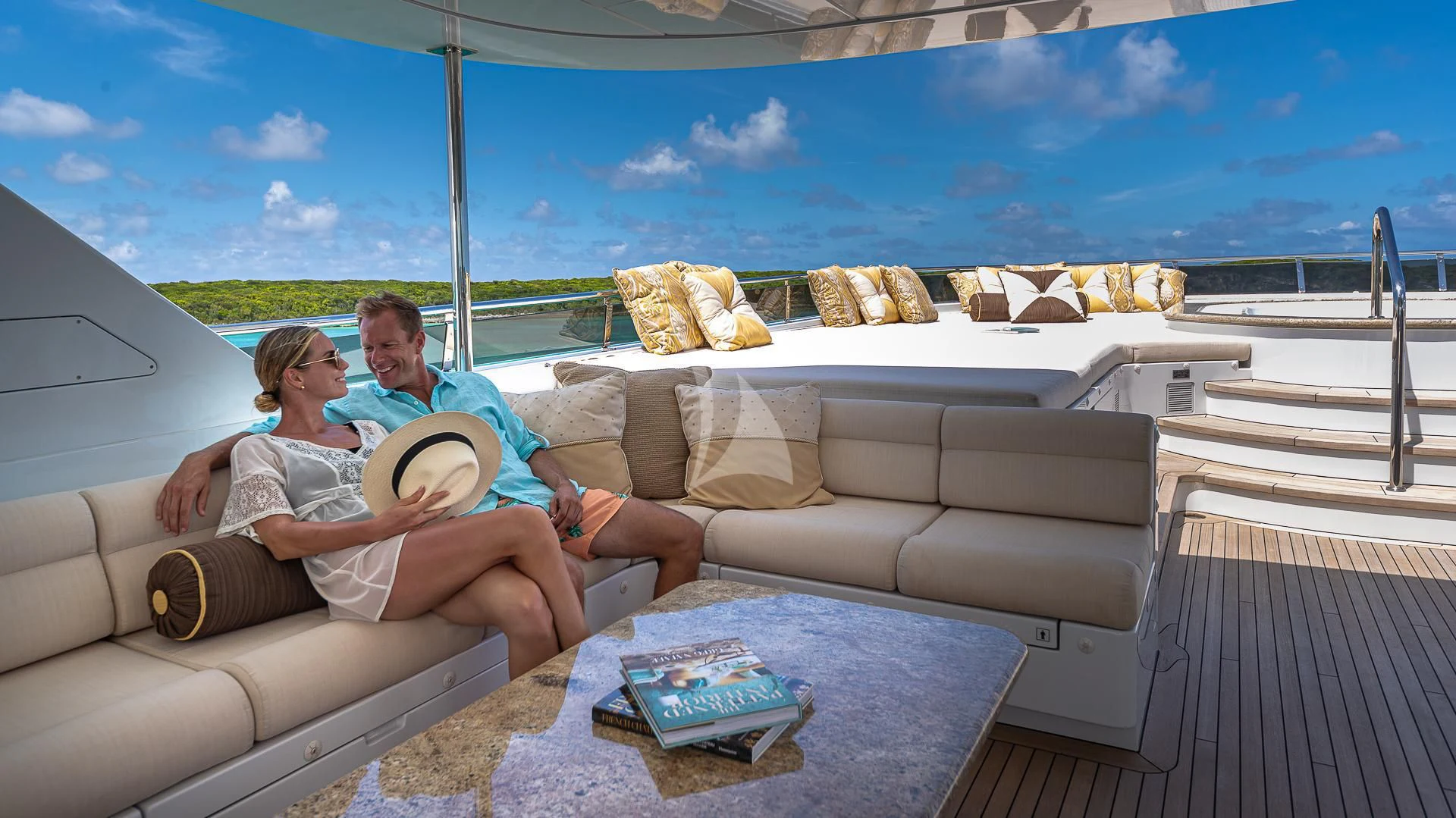 a man and woman sitting on a couch on a deck with a pool and blue sky aboard SILVER LINING Yacht for Sale