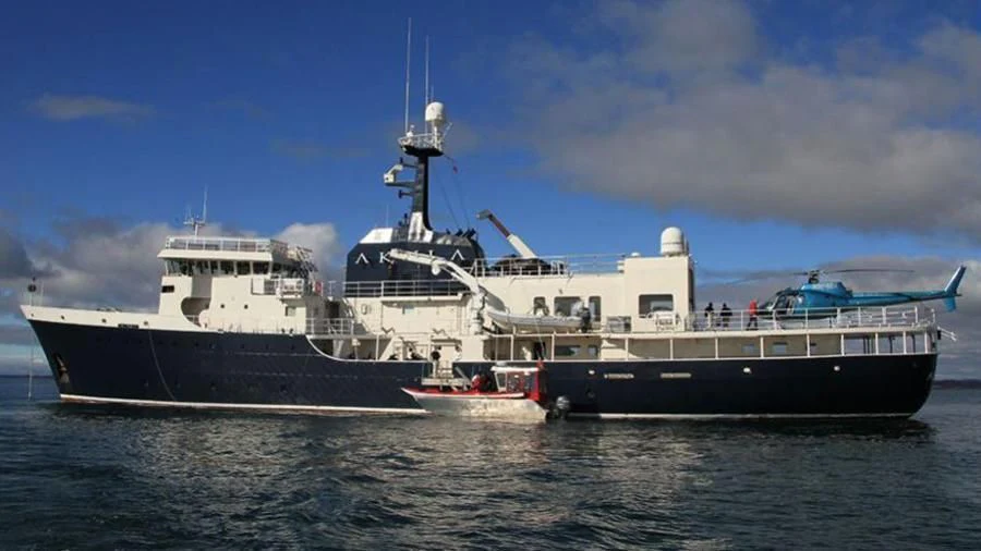 a large ship with a smaller boat in the water aboard OMNIA Yacht for Sale