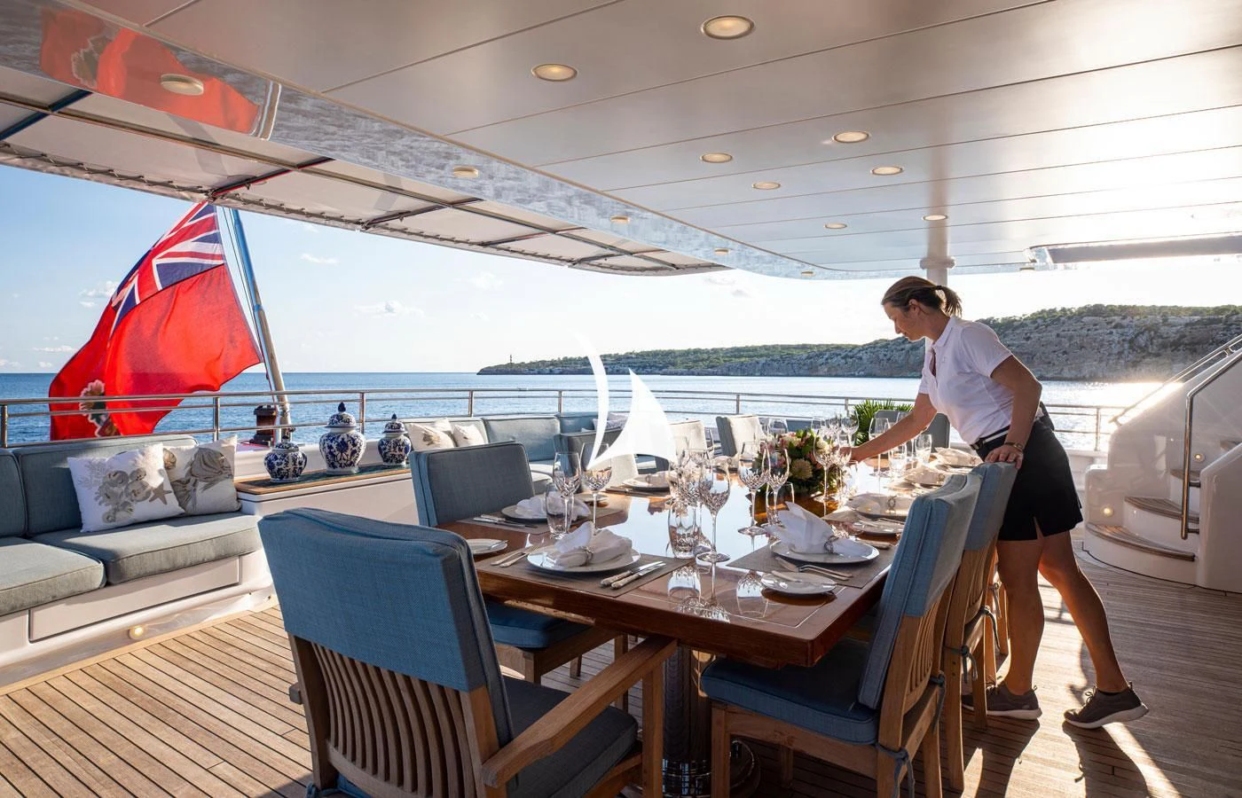 a man standing on a deck near a table with a red flag aboard EMERALD (YET) Yacht for Sale