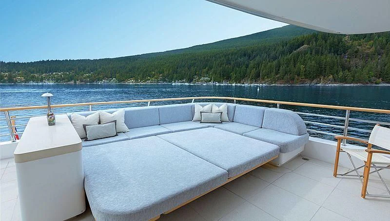 a large white couch with a glass of wine on a patio by a body of water aboard KOJU Yacht for Sale