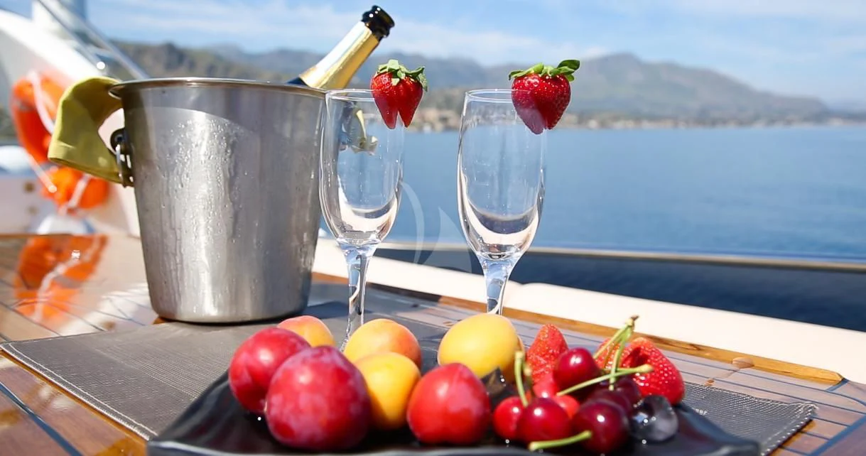 a glass of wine next to a bowl of fruit on a table aboard JAUNI Yacht for Sale