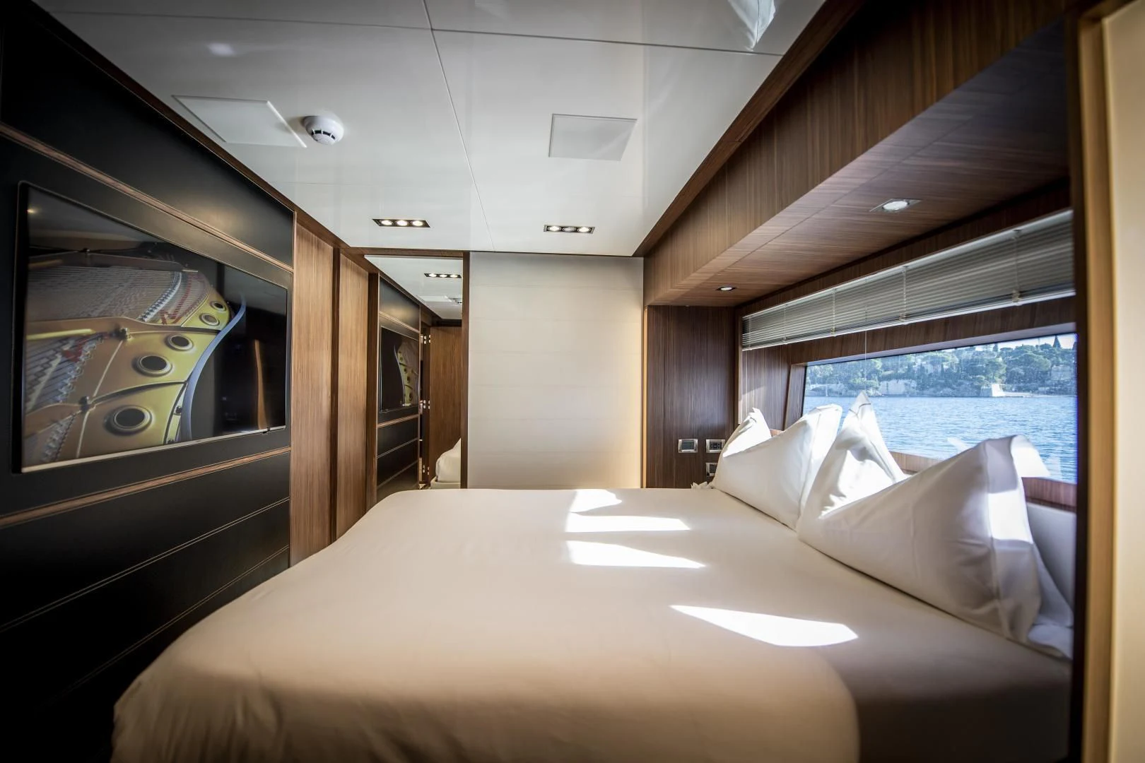 a bed with a white sheet and pillows in a room with a window aboard WILDONE Yacht for Sale