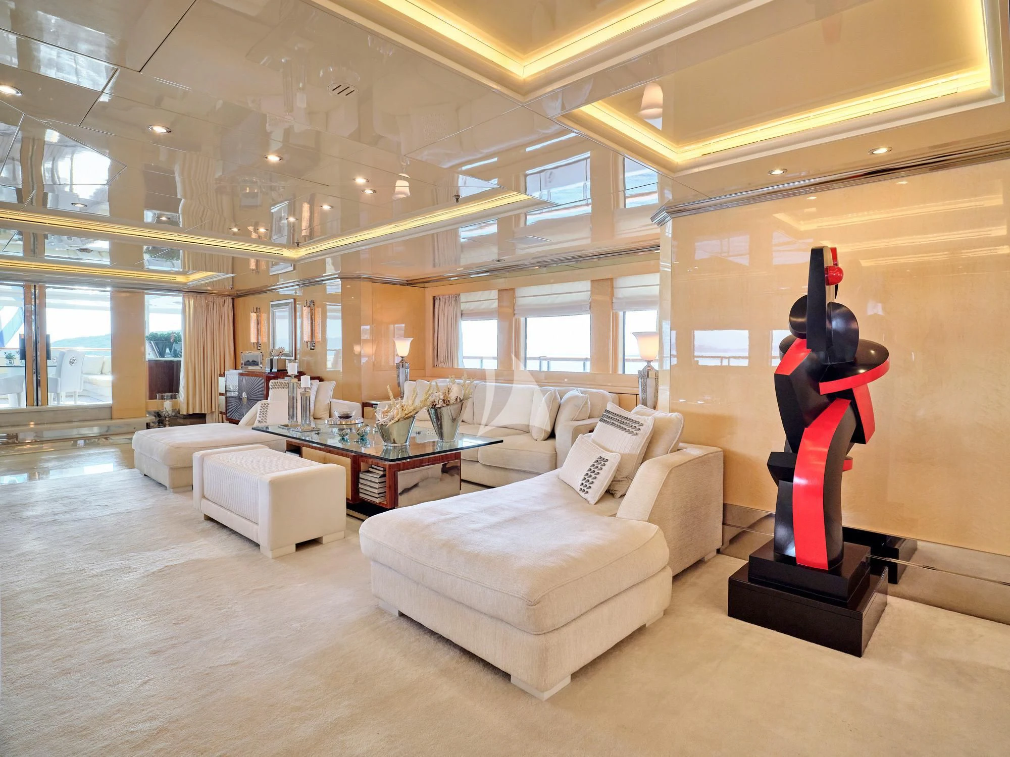 a person in a red suit standing on a white couch in a large room with large windows aboard SUNDAY Yacht for Charter
