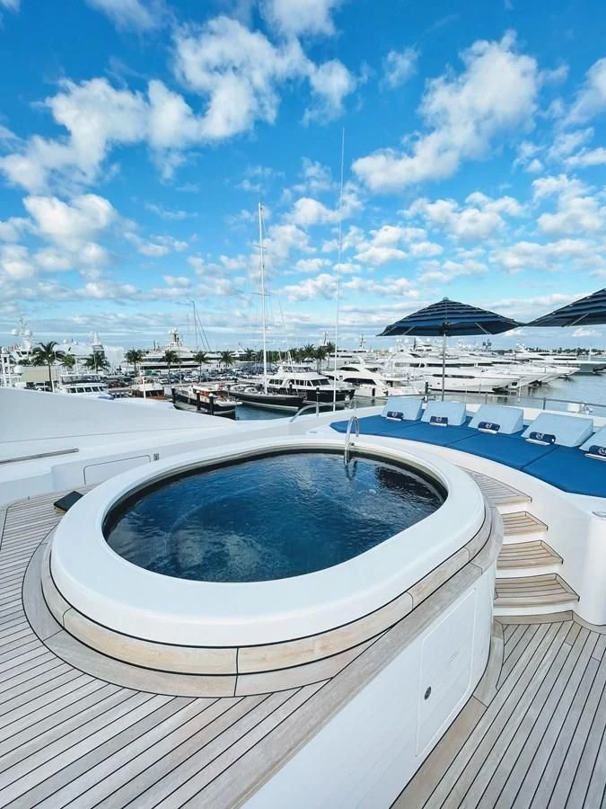 a pool with a deck and lounge chairs on a deck with a beach and water and blue sky aboard NEXT CHAPTER Yacht for Sale