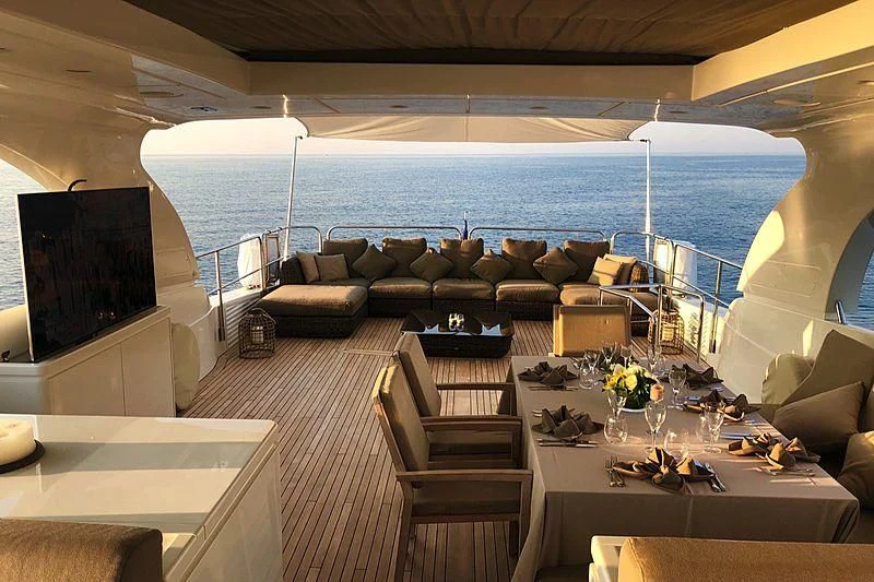 a room with a large sofa and a table with chairs and a television aboard FASTER Yacht for Sale