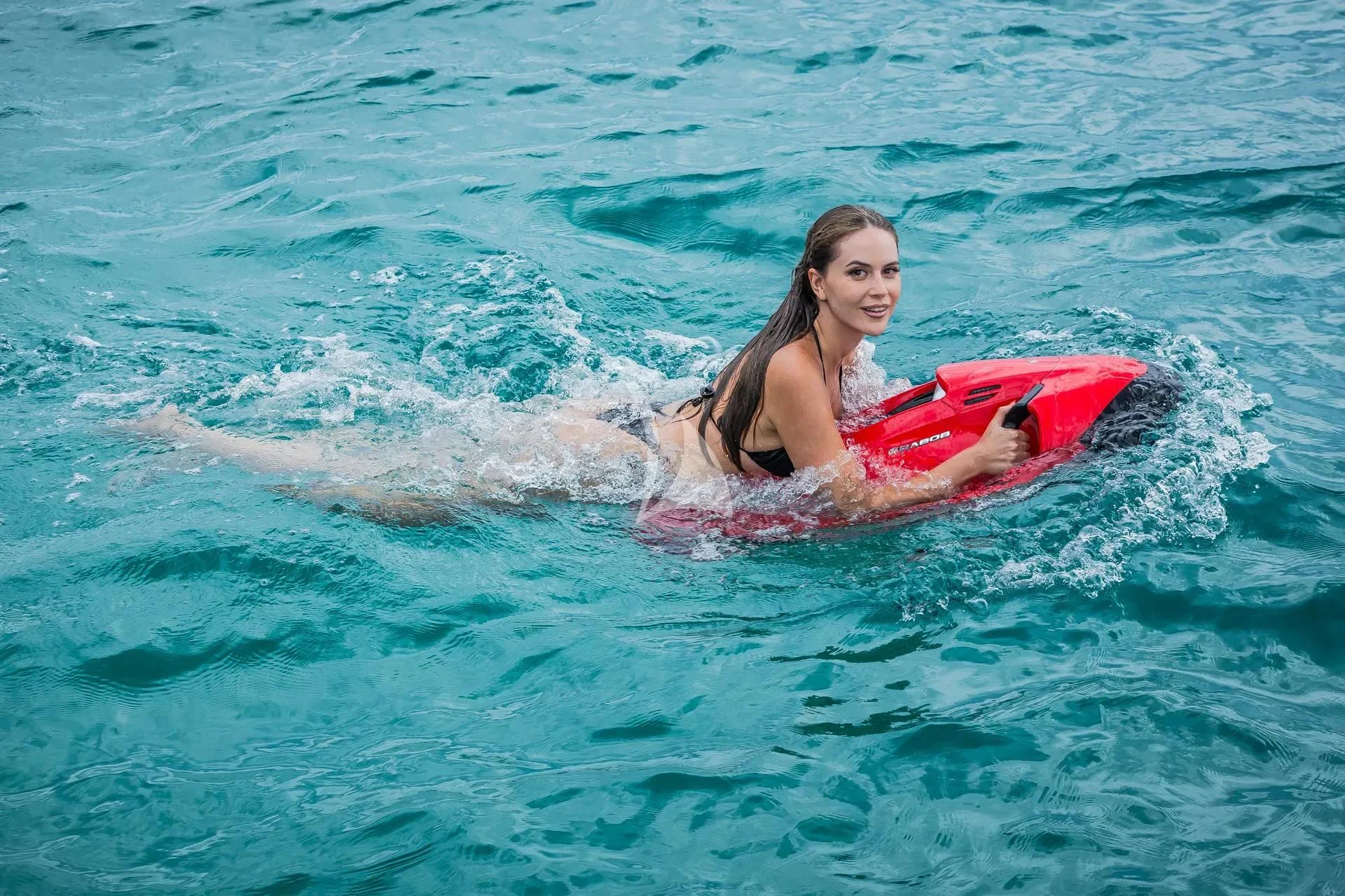 a person in the ocean holding a red surfboard aboard KARISMA Yacht for Sale