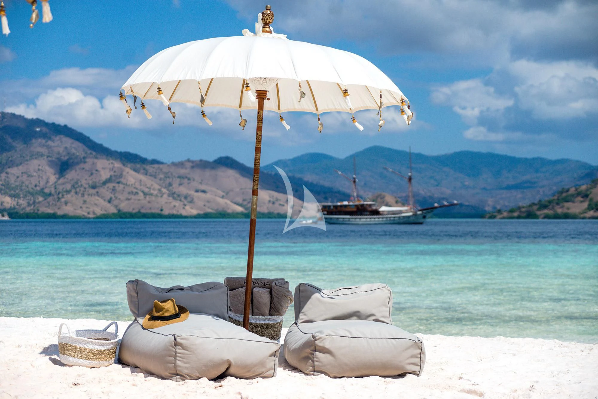 a beach with a large umbrella and a couple of boats on it aboard PRANA Yacht for Charter