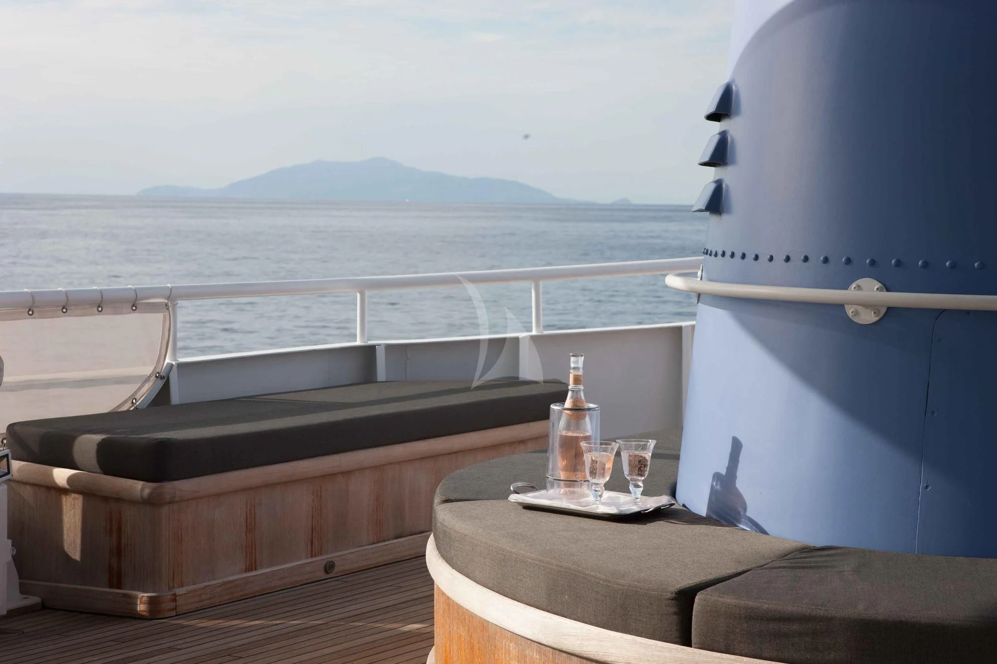 a table with a bottle of wine on it and a view of the ocean and mountains in the aboard ICE LADY Yacht for Sale