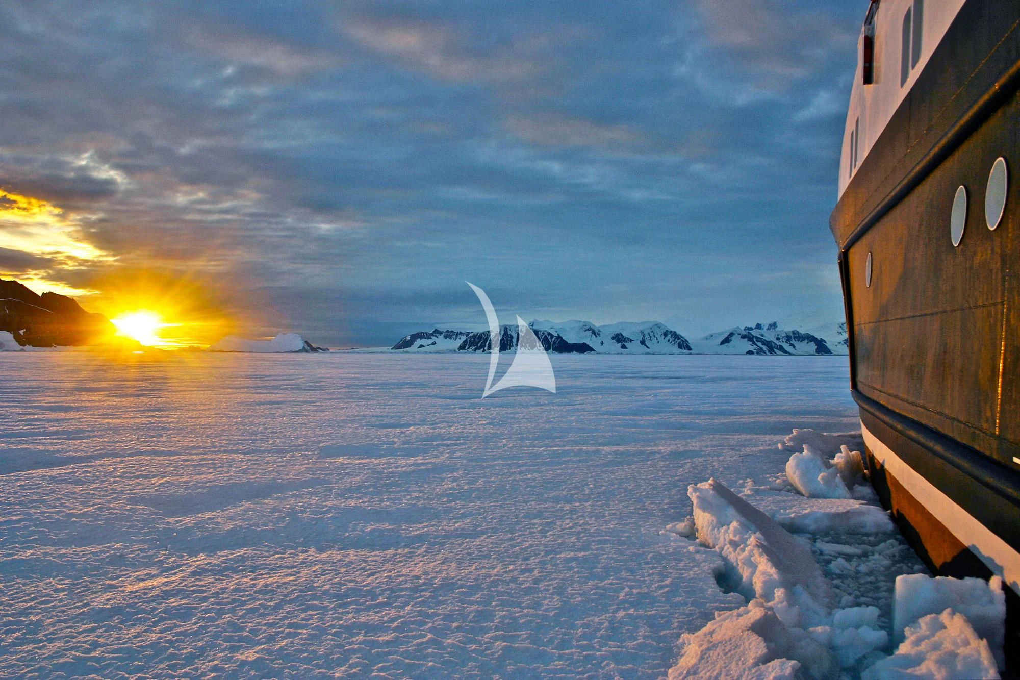 a snowy landscape with a building and mountains in the background aboard HANSE EXPLORER Yacht for Sale