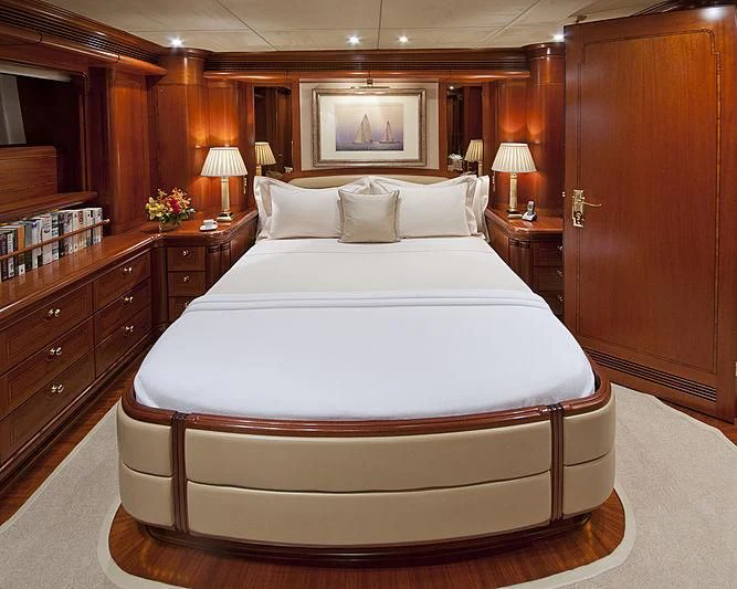 a bed with a white sheet and pillows in a room with wood cabinets aboard HYPERION Yacht for Charter