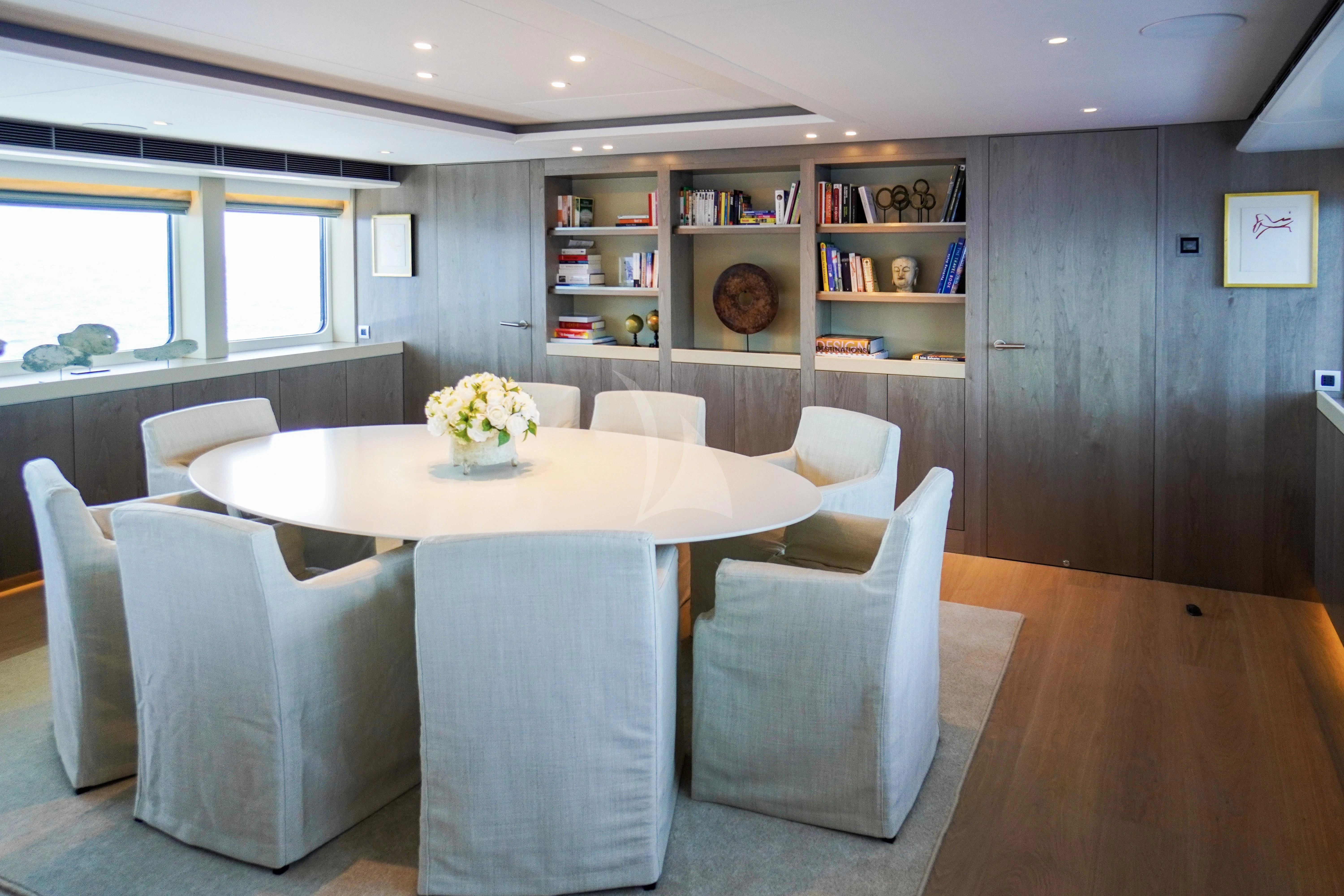 a room with a table chairs and a shelf with books aboard UNEXPECTED Yacht for Sale