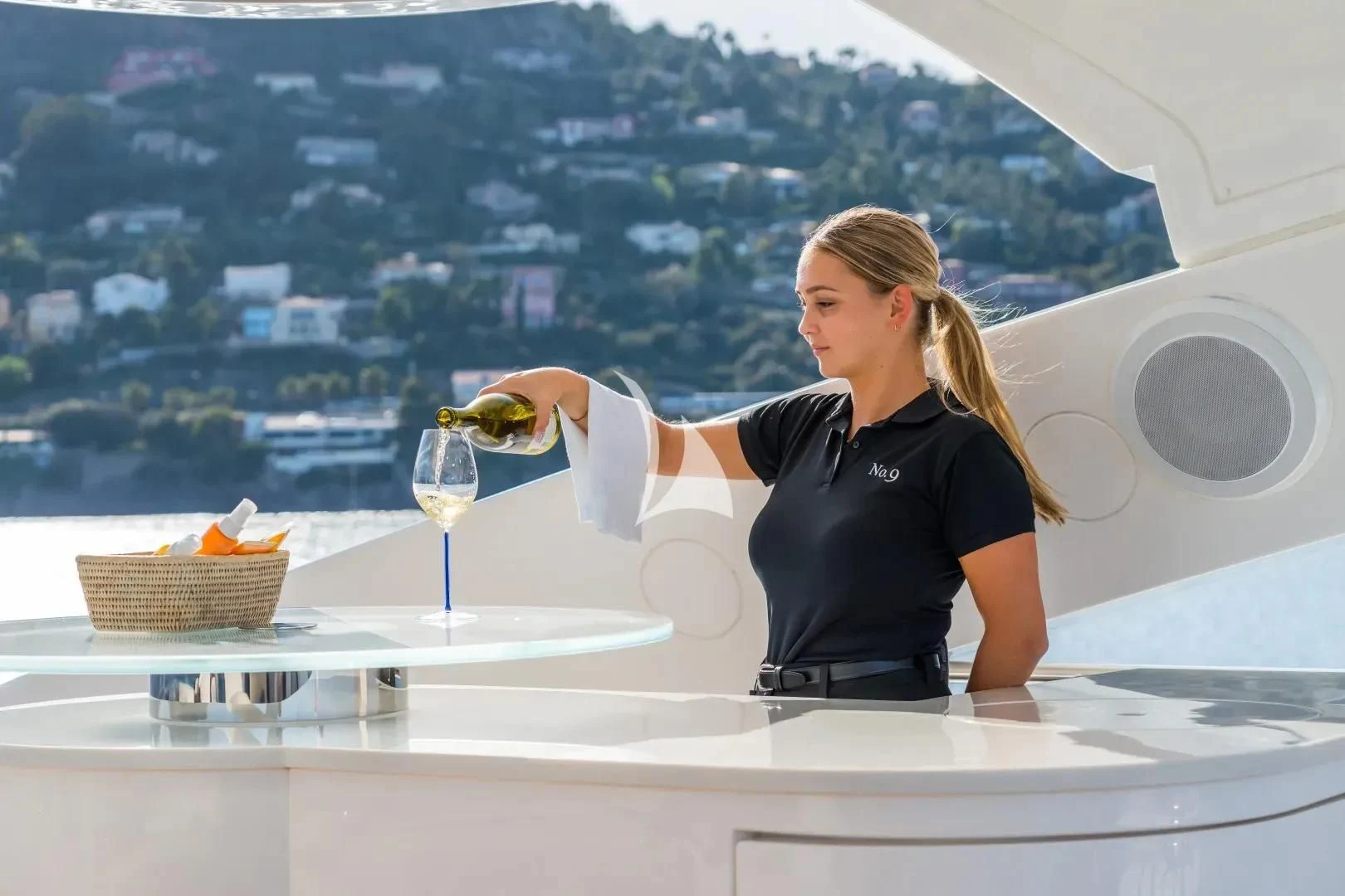 a woman sitting at a table with a glass of wine and a city in the background aboard NO.9 Yacht for Sale