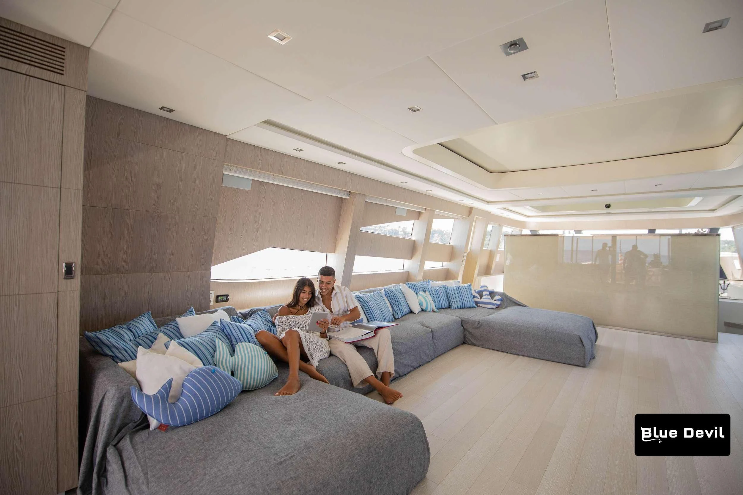 a couple of people sitting on a couch in a room with a wood door and a white ceiling aboard BLUE DEVIL Yacht for Sale