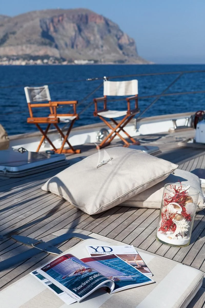 a table with a couple chairs on it by a beach with a mountain in the background aboard LOTTY Yacht for Sale